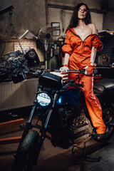 Attractive sexual young woman in orange jumpsuit staying on modern motorcycle in the car service