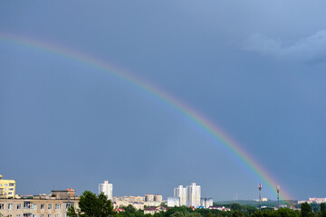 Bright multicolored rainbow on the houses of the city in the blue sky