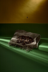 Kaffeebohne fällt auf Haufen mit Kaffeebohnen auf Jute Stoff mit grünem Tisch auf gelben Hintergrund und Sonnenstrahlen