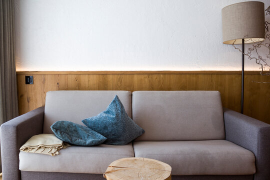 Modern hotel lounge interior with comfortable sofa and pillows. Cozy alpine chalet living room design with rustic wooden wall paneling, led backlight and contemporary furniture