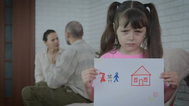 Family conflict. Sad little girl with a picture on the background of parents quarreling with each other.