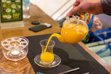 man's hand pours sea oange tea from glass teapot into a cup of glass. close-up, soft focus, blur background