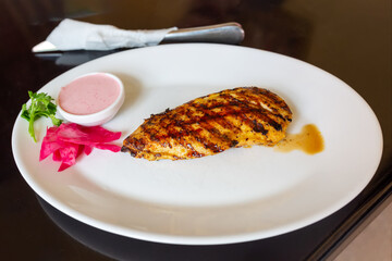 Appetizing grilled chicken breast on a white plate with pink sauce