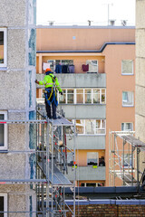 the worker assembles the scaffolding on the facade of a multi-storey house at a dangerous height