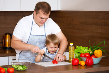 Happy father teaches son to cut salad in the kitchen