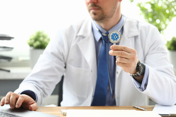 A male doctor sits in a clinic and shows a stethoscope. Coronavirus infection symptoms concept