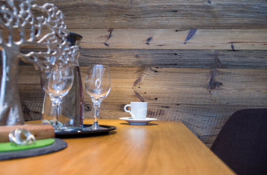 Cozy restaurant table setting with wine glasses and coffee cup. Elegant alpine hotel dining interior with rustic wooden wall background, hospitality and comfort concept.