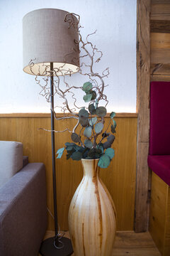 Cozy hotel lounge interior corner with floor lamp and floor vase. Elegant alpine chalet room decoration with rustic wooden wall paneling, modern lamp light and comfortable atmosphere.
