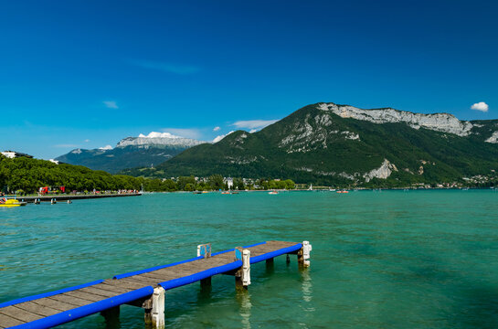 View of Annecy lake,wooden pier,boats with tourists and Alps mountains on sunny day with blue sky in Annecy city.Annecy is the largest city of Haute-Savoie department in France.