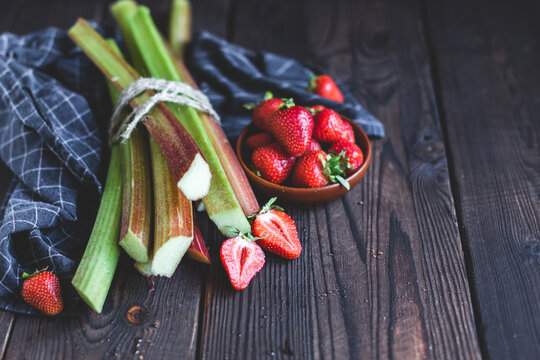 Fresh organic garden strawberries and rhubarb stems on wooden background. Flat lay. Ingredients for summer lemonade, jam or cake