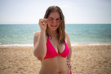 young playful caucasian girl laughing and looking at the camera, dressed in a pink bikini and glasses hearts.