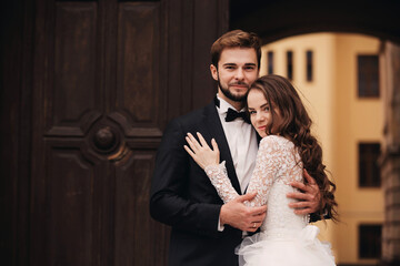 Happy newlywed couple hugging and kissing in old European town street, gorgeous bride in white wedding dress together with handsome groom. wedding day