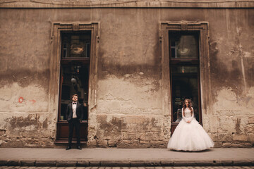 Happy newlywed couple on a walk in old European town street, gorgeous bride in white wedding dress together with handsome groom