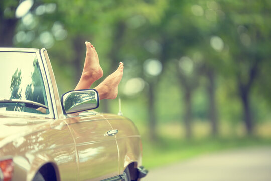 Bare feet sticking out of a cabrio vintage car parked in the nature