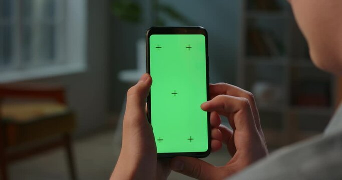 Close up shot of guy using his smart phone with mock up green screen at night, using various gestures to scroll through online shop or social media 4k video template