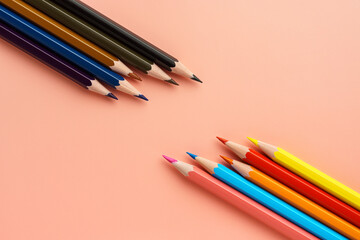 Fototapeta premium Set of colored bright pencils lie opposite dark pencils on pink pastel background, flat lay. Pencils lie diagonally in the lower right and upper left corner.