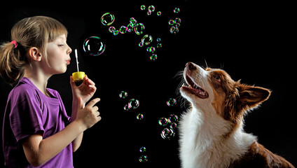 little girl blowing soap bubbles and her dog playing with them - black background