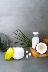 Open spa cream for body skincare and hair with coconut oil, fresh coconuts, palm leaf and bottle with coconut butter on dark gray background. Natural cosmetics concept. Vertical card. Copy space