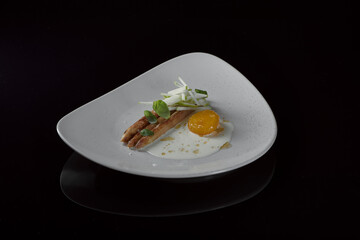 vegetarisches Spargel Gericht mit gebeiztem Eigelb, grünem Apfel und Basilikum Sauce auf cremefarbenen Teller und schwarzer reflektierender Oberfläche