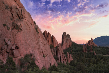 Garden of the Gods with colorful pink and purple sunset. Beautiful colors cast light on the rock formations in colorado springs. Colorful clouds, green trees, and orange rocks visible