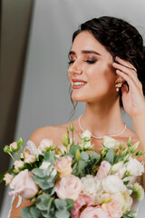 Bride with wedding bouquet smiles and touches her face and hair. Attractive girl portrait for social networks. Girl in wedding gown on blank background. Dreamily bride woman