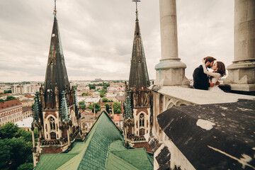 Happy newlywed. beautiful bride and stylish groom are kissing on the balcony of old gothic cathedral with panoramic city views