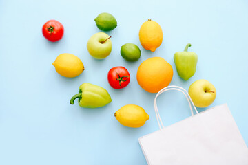 Various fresh vegetables and fruits on blue background. Shopping concept. Tomatoes, peppers, lemons, apple and lime scattered from shopping bag, top view