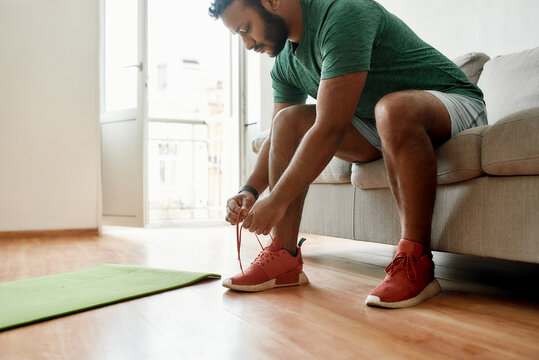 Get ready. Cropped shot of young man in sneakers tying shoelaces, preparing for morning workout on a yoga mat at home. Fitness, motivation concept