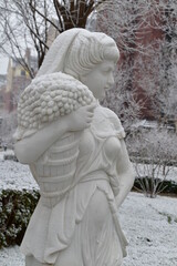 Beautiful female greek statue covered in snow in Christmas eve winter garden