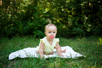 a little girl with a pacifier is on all fours on a blanket in nature