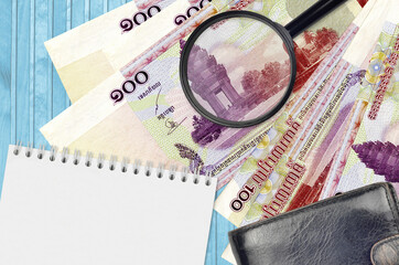 100 Cambodian riels bills and magnifying glass with black purse and notepad. Concept of counterfeit...