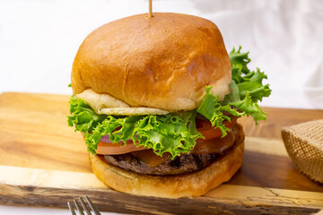 A view of a cheeseburger on a rustic wooden cutting board, in a restaurant or kitchen setting.