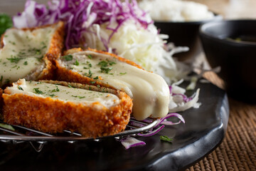 A closeup view of a plate of cheese katsu, in a restaurant or kitchen setting.