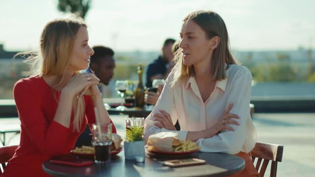 Beautiful two women resting talking drinking cocktail eating burger in summer cafe street sisters cafe casual city friendship models outdoors slow motion