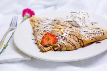 A view of a French crepe, featuring fruit, powdered sugar and chocolate syrup.