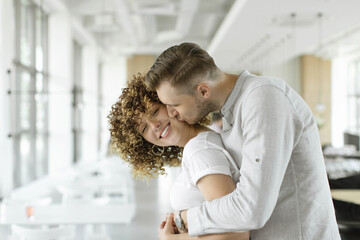 Happy couple, husband and wife are hugging in a cafe against a background of light walls. The husband kisses his wife. Close-up.