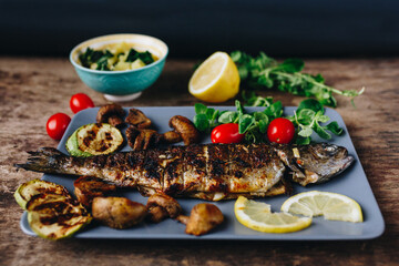 Grilled trout fish with lemon, herbs, mushrooms and tomato on wooden table