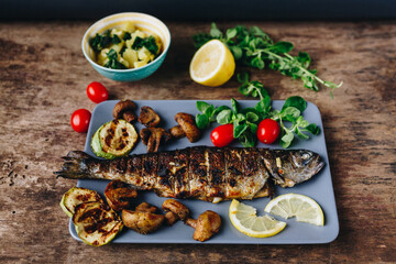 Grilled trout fish with lemon, herbs, mushrooms and tomato on wooden table