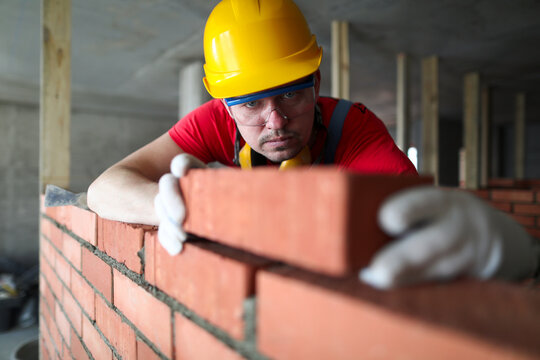 Builder carefully puts red brick on the masonry