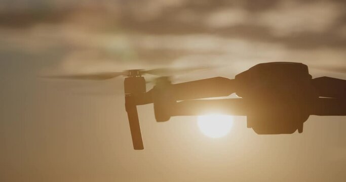 Silhouette of drone flies against bright sky in evening or morning. Modern technologies for shooting photos and videos from above. Sunset, sunrise, golden hour. Drone backlit in sunshine light