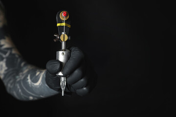 Artist with professional tattoo machine on black background, closeup. Space for text