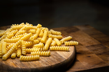 Uncooked curly pasta on wooden table background. Stack of traditional dry raw macaroni. Nobody