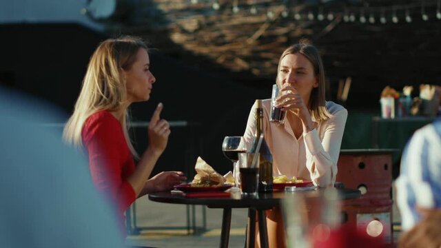 Two women resting talking use phone drinking cocktail eating french fries in summer cafe street sisters cafe casual city friendship models outdoors slow motion