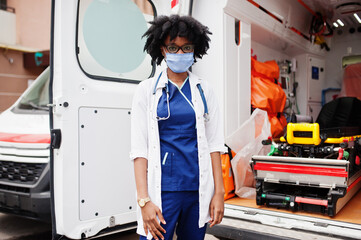 African american female paramedic in face protective medical mask standing in front of ambulance car. © AS Photo Family
