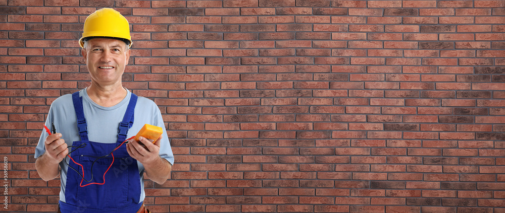 Wall mural electrician with multimeter near brick wall, space for text. banner design