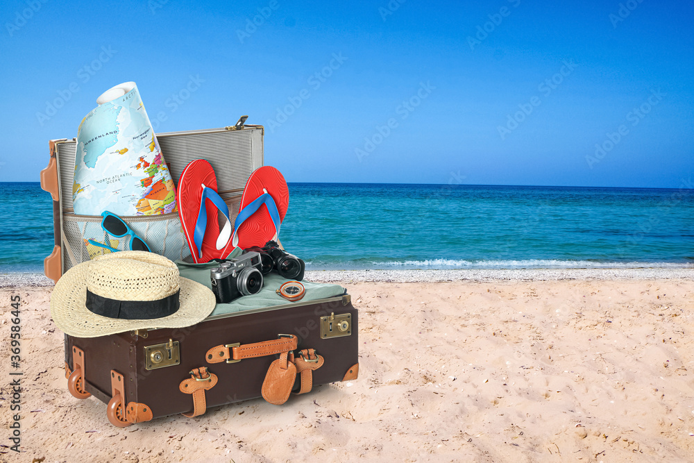 Wall mural Open vintage suitcase packed for summer vacation on sandy beach. Space for text