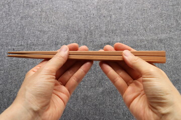 Hands holding wooden chopsticks on gray background
