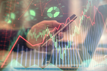 Double exposure of man's hands holding and using a phone and financial graph drawing. Analysis concept.