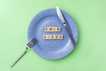 Words Fuck diet. Wooden blocks with lettering on empty plate surrounded by knife and fork on green...