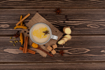 Top view on traditional indian drink masala chai, tea with milk and spices in the form of cinnamon stick, green cardamom, ginger, anise star and others on wooden background